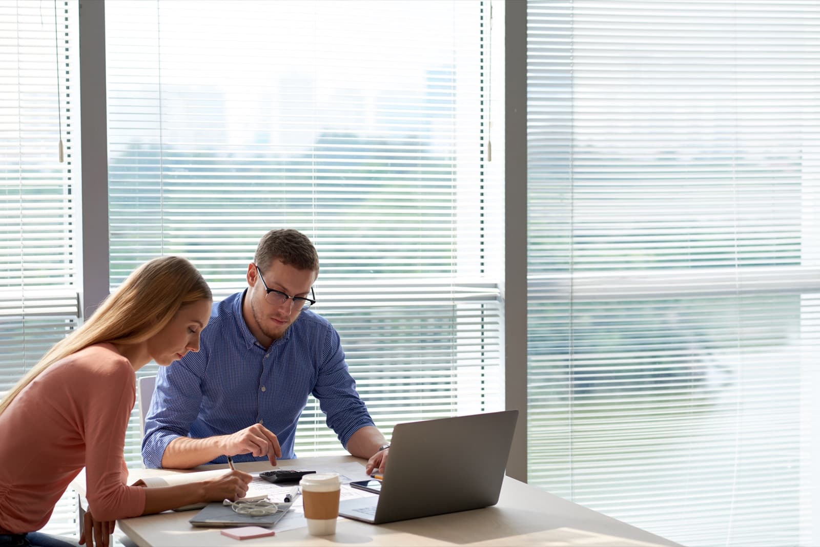 Two colleagues working through a project on a laptop beside an office window