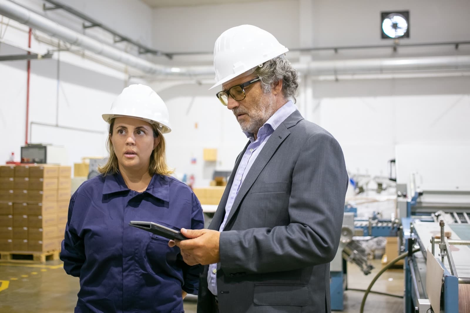 An engineer and a plant worker in hard hats talking on a factory floor